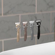 four razors in different colors are hanging on a wall next to a sink and tiled walls