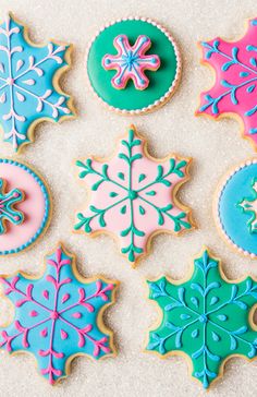 decorated cookies are arranged in different colors and shapes on a white tablecloth with snowflakes