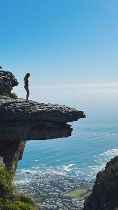 a woman standing on top of a cliff next to the ocean