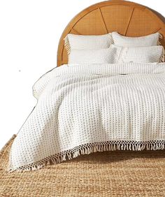 a bed with white linens and pillows on top of it, in front of a wooden headboard