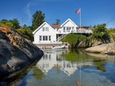 a white house sitting on top of a hill next to a body of water with a boat in front of it