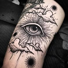 an all seeing eye tattoo on the left arm with stars and clouds around it in black ink