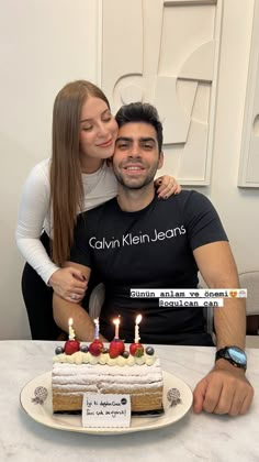 a man and woman sitting in front of a cake with lit candles on it,