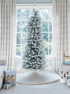 a white christmas tree sitting in front of a window next to a box and presents