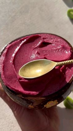 a hand holding a spoon in a bowl filled with red liquid and green peppers on the side