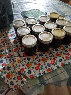 a table topped with lots of jars of food on top of a flowered cloth