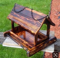 a wooden birdhouse with chain hanging from it's roof on a bench in the grass