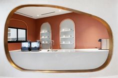 an oval mirror reflecting the interior of a bathroom with orange walls and white countertops