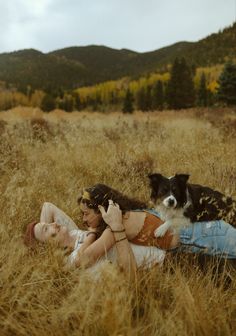 a woman laying in the grass with a dog on her lap and another person holding a cell phone up to her ear