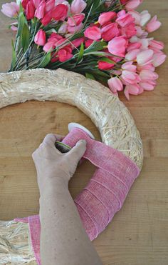 someone is making a wreath out of wicker and fabric with pink flowers in the background