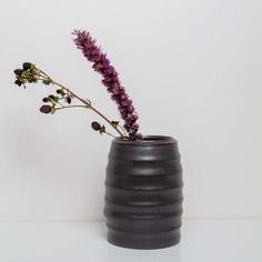 a purple flower in a black vase on a white tableclothed surface with space for text