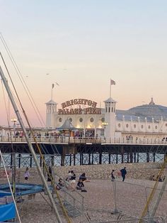 people are sitting on the beach next to boats and piers in front of a white building