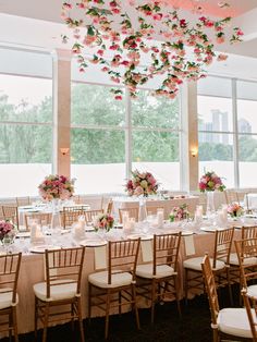 wedding reception tables with pink and white flowers hanging from the ceiling, and in front of large windows