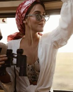 a woman wearing glasses and a red bandana is sitting in a car looking out the window