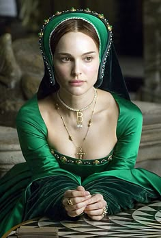 a woman in a green dress sitting on a stone bench wearing a tiara and necklace