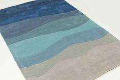 an area rug with blue, grey and white waves on the top is shown in front of a white background