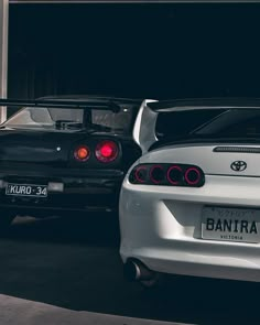 two cars parked next to each other in front of a garage with their lights on