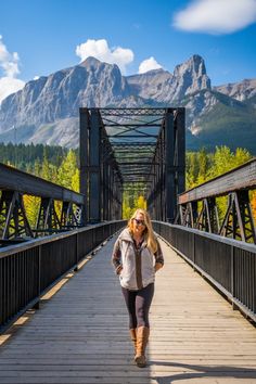 a woman walking across a bridge with mountains in the background