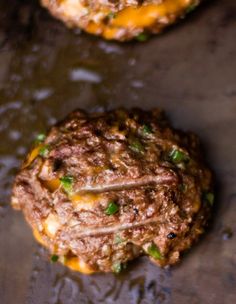 two hamburger patties with cheese and green onions on a baking sheet, ready to be eaten