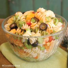 a glass bowl filled with pasta salad on top of a green place mat next to silverware