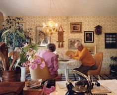 two people sitting at a table in an old fashioned room with flowers on the desk