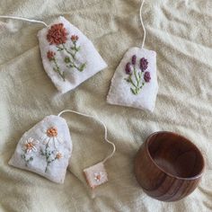 three handmade tea bags with flowers on them next to a wooden bowl and string