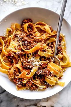 a white bowl filled with pasta covered in meat and sauce on top of a marble table