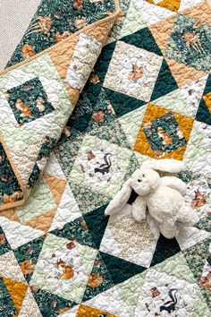 a white teddy bear sitting on top of a quilt