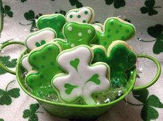 green and white decorated cookies in a bowl on a tablecloth with shamrocks around it