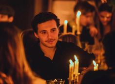 a man sitting at a table with candles in front of him and people around him