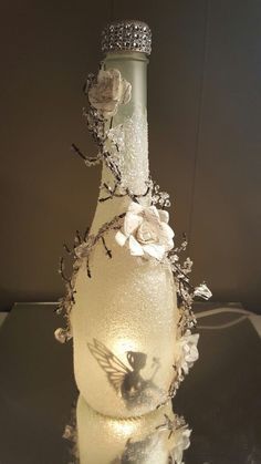 a glass bottle with flowers on it sitting on a table next to a light bulb