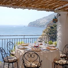 an outdoor dining area overlooking the ocean and mountains with tables set up for two on it