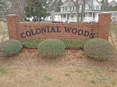 the sign for colonial woods is shown in front of a brick wall and some bushes