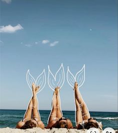 three women laying on the beach with their legs up in the air and leaves above them