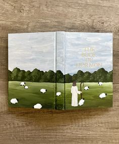 the book of mormon is open on a wooden surface with sheep grazing in the field