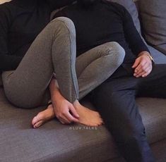 a woman sitting on top of a gray couch next to a man in black shirt