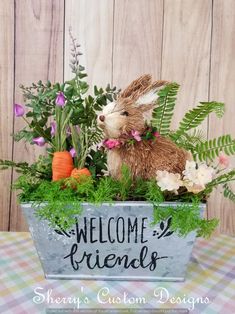 a welcome sign with a bunny sitting in the center surrounded by flowers and greenery