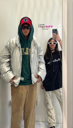 two people standing next to each other in front of a white wall wearing sunglasses and jackets