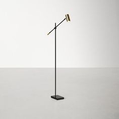 a black and gold floor lamp on a white surface with an empty wall in the background