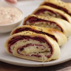 a white plate topped with meat and cheese roll next to a bowl of ranch dressing