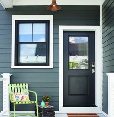 a green chair sitting in front of a black door on a gray house with white trim