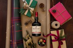 a bottle of red wine surrounded by presents and wrapping paper on a table with christmas decorations