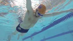 a man swimming in a pool with a ball on his head and wearing swim trunks