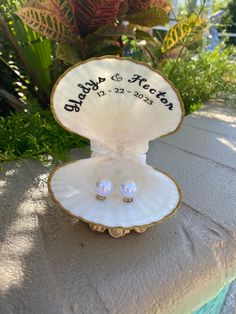 an open shell with two pearl studs in it sitting on a table next to some plants