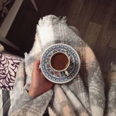 a person holding a cup of coffee on top of a blanket