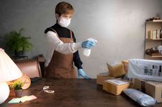 a man in an apron and face mask is cleaning a table with gloves on it