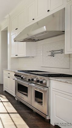 a kitchen with white cabinets and stainless steel stove top oven in the center of the room