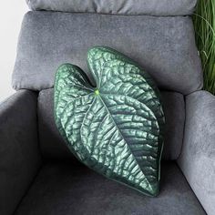 a green leaf shaped pillow sitting on top of a gray couch next to a plant