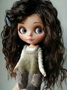 a close up of a doll with long brown hair and big eyes wearing a sweater