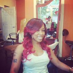 a woman with pink hair sitting in front of a mirror and smiling at the camera